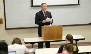 HSU professor standing behind a podium with a document in hand speaking to his students