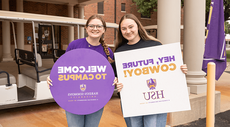 Two tour guides holding up signs to welcome new students.